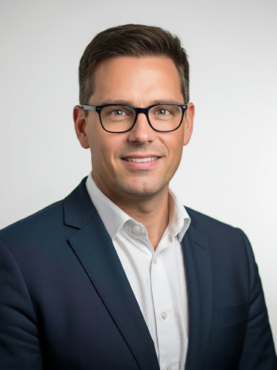 Professional business headshot of a man in a navy suit and glasses