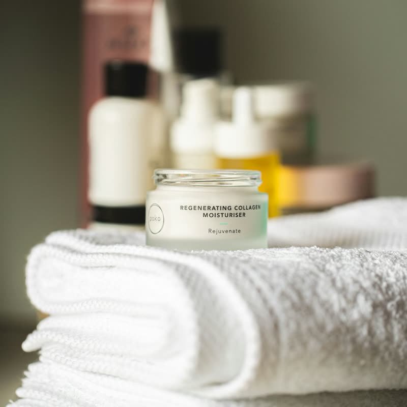 Face cream jar on a white towel with skincare bottles behind