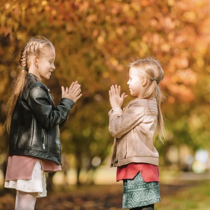 Sisters playing a clapping game in autumn