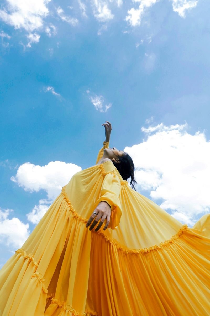 Model in a flowing yellow gown against a blue sky