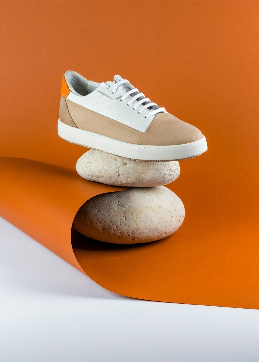 Suede sneaker balanced on stones against an orange backdrop